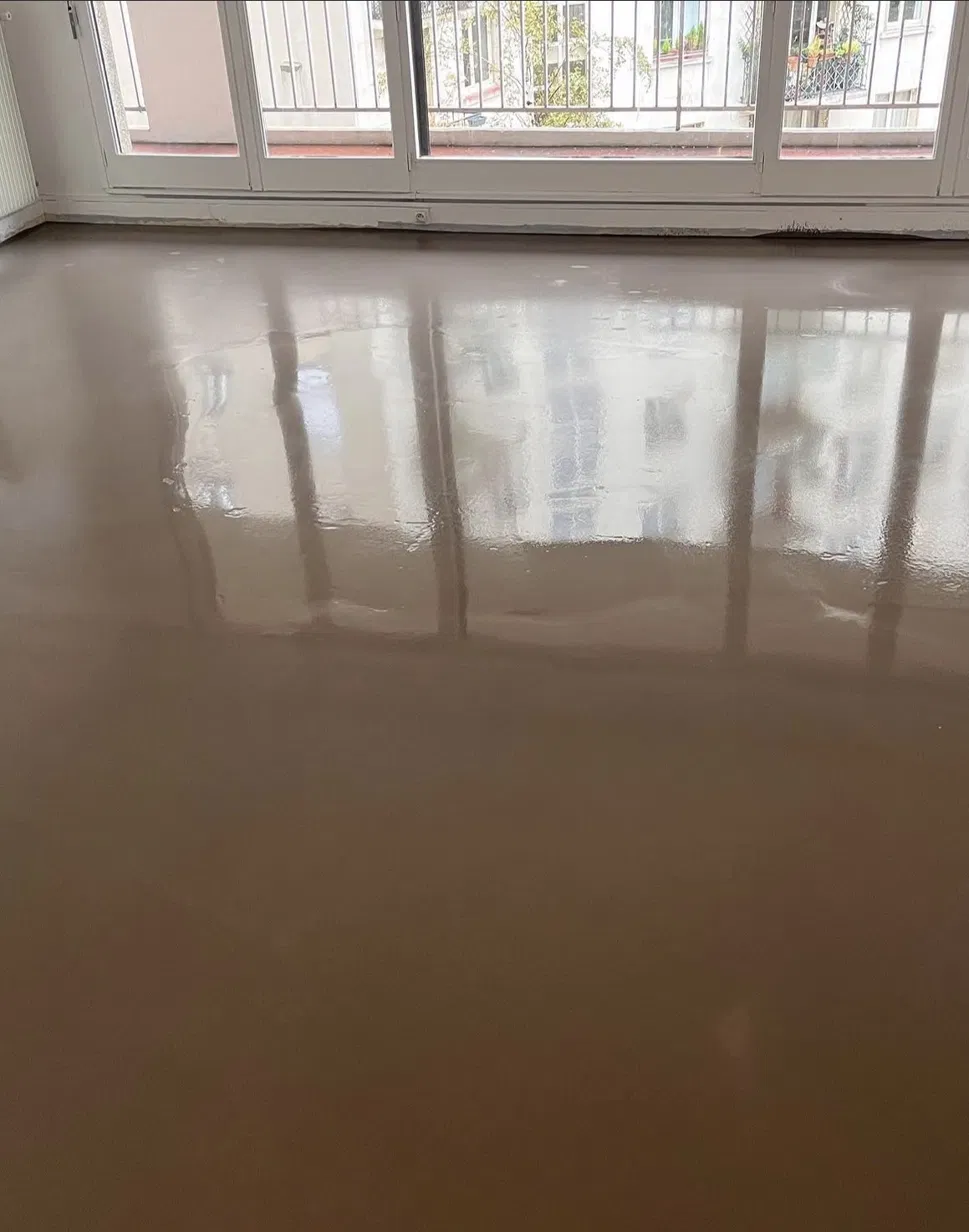Ragréage fraîchement coulé, encore brillant, avant la pose du parquet
