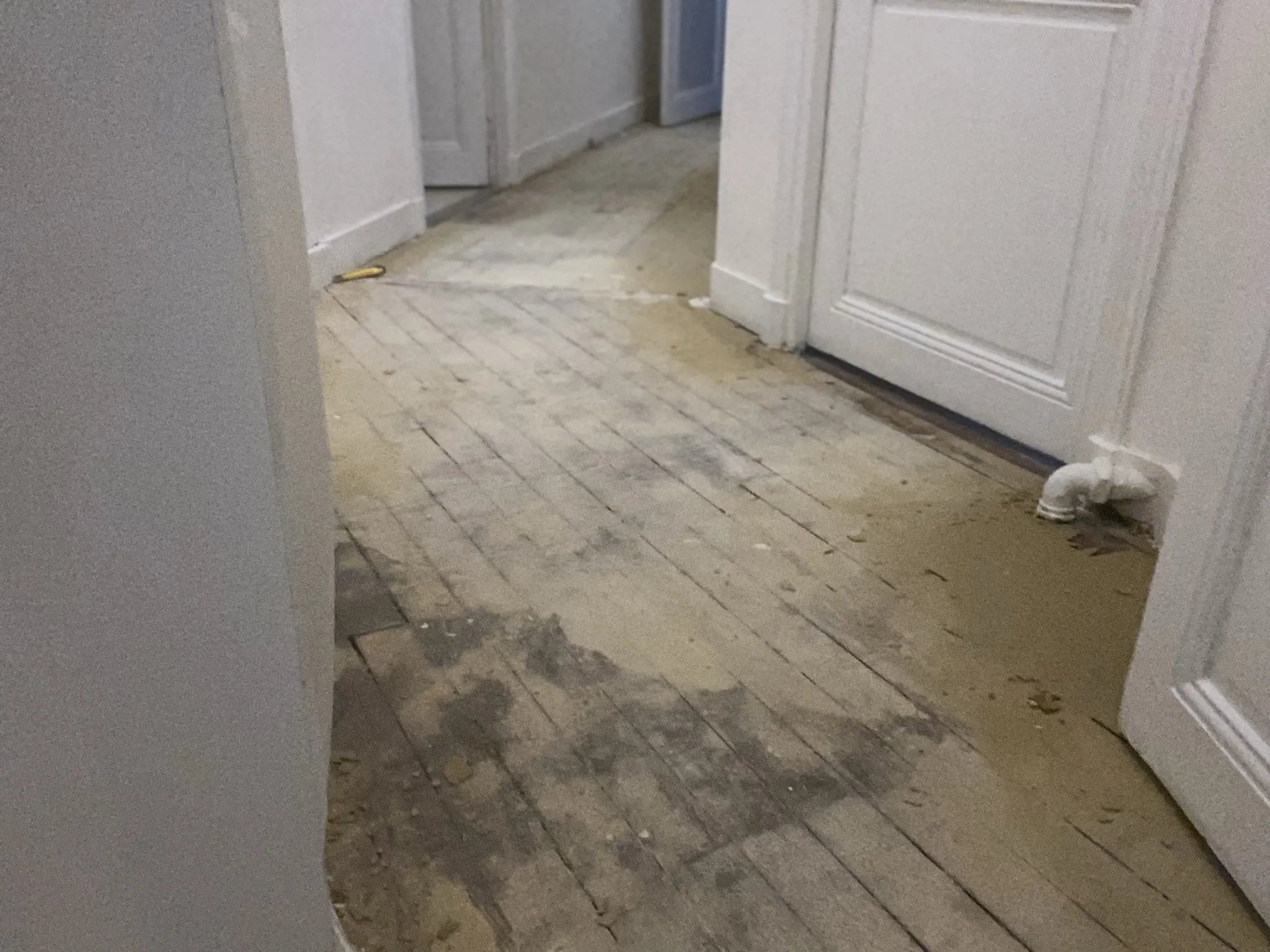 Couloir avant travaux : lames de parquet nues et usées, interstices ouverts entre les lames