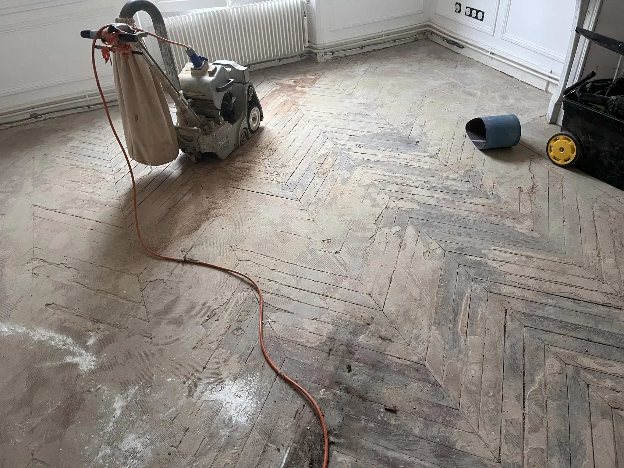 Ponçage du parquet en chevrons à la ponceuse à bande, radiateur en fonte