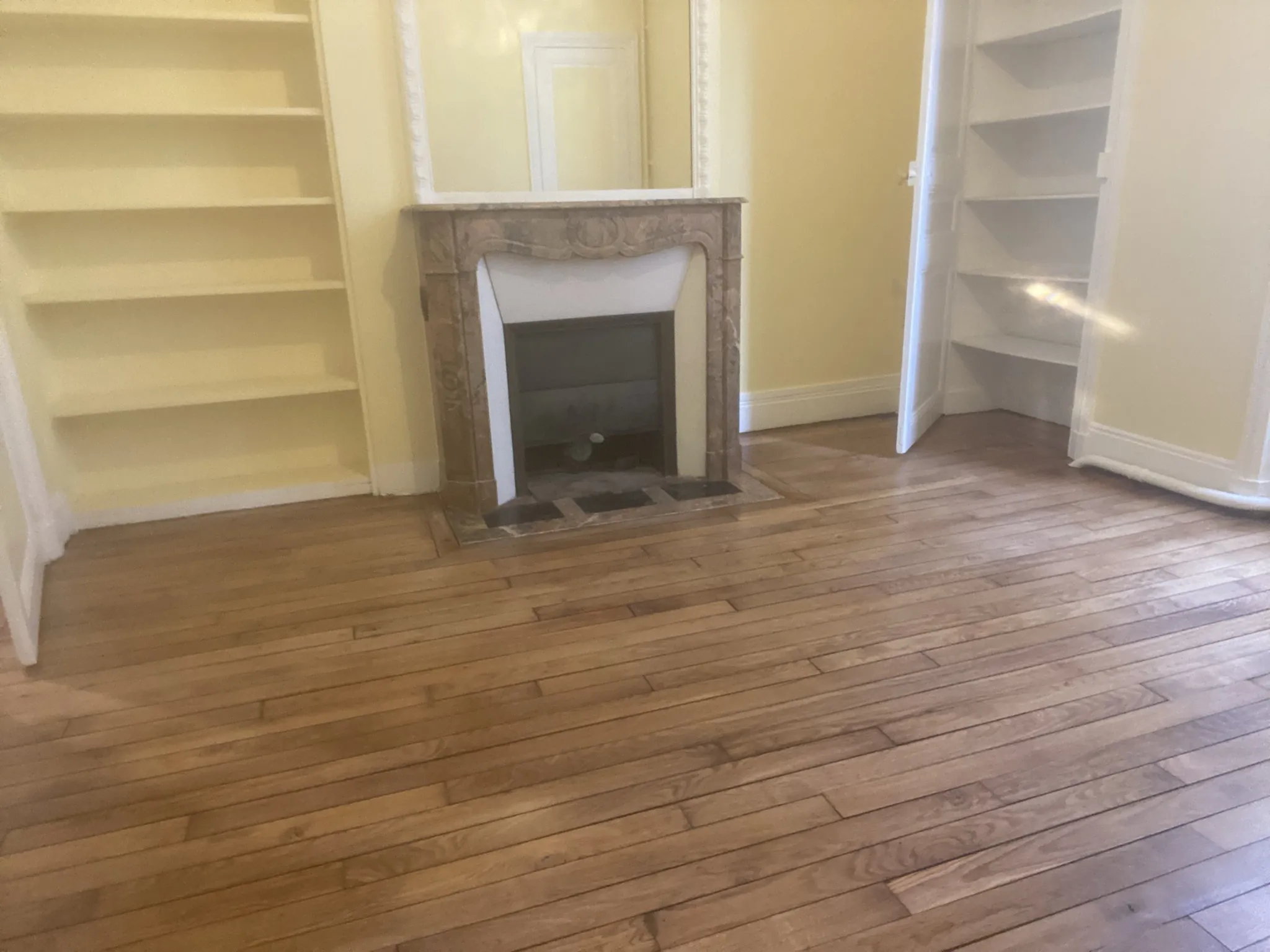 Pièce avant travaux : murs jaunes, cheminée encadrée d'étagères, parquet terni